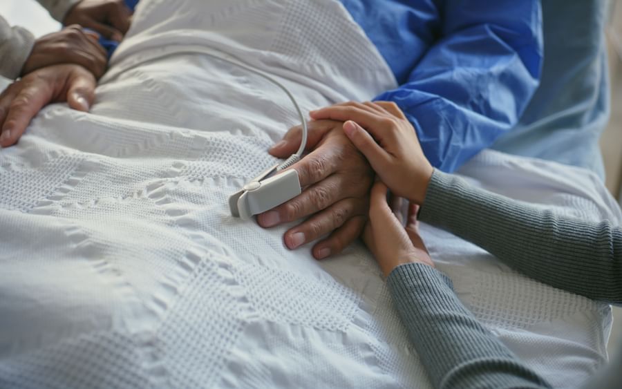 Caregivers cradle a patient’s hand on a white blanket with a monitor strapped to the abdomen.