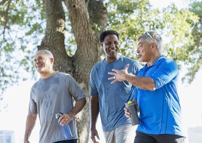 Three people walking and chatting outdoors near a tree, with water bottles.