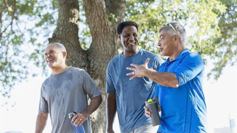 Three people walking and chatting outdoors near a tree, with water bottles.