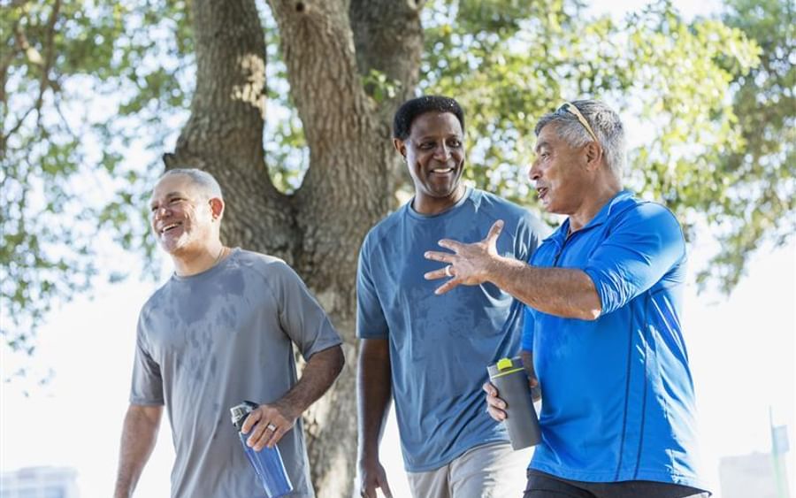 Three people walking and chatting outdoors near a tree, with water bottles.