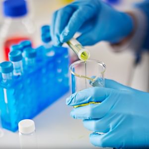 Gloved hands pipette greenish-yellow liquid into a test tube.