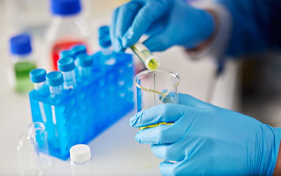 Gloved hands pipette greenish-yellow liquid into a test tube.
