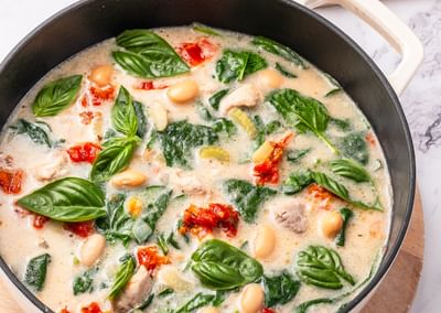 Creamy spinach and white bean soup with basil, red peppers, and bread slices on a wooden board.