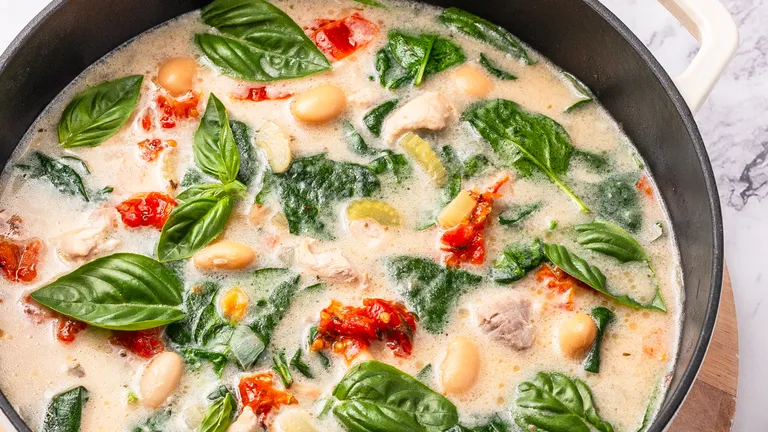 Creamy spinach and white bean soup with basil, red peppers, and bread slices on a wooden board.