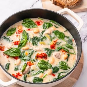 Creamy spinach and white bean soup with basil, red peppers, and bread slices on a wooden board.