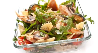 Bow-tie pasta salad with grilled chicken, mushrooms, arugula and tomatoes in a glass dish