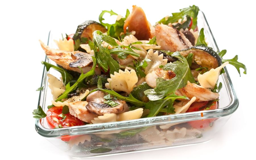 Bow-tie pasta salad with grilled chicken, mushrooms, arugula and tomatoes in a glass dish
