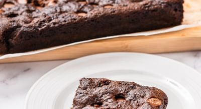 Rich chocolate brownie with nuts on a white plate, slice cut on a marble surface.