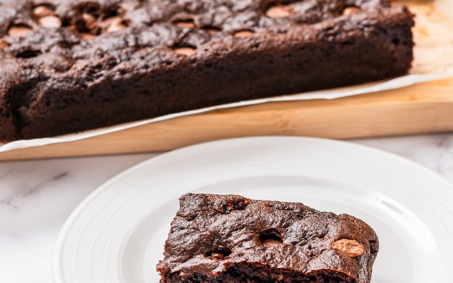 Rich chocolate brownie with nuts on a white plate, slice cut on a marble surface.