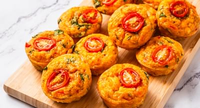 Golden savoury bites topped with cherry tomato halves on a wooden board.