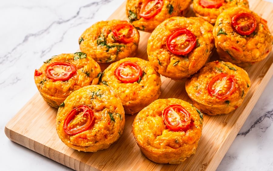 Golden savoury bites topped with cherry tomato halves on a wooden board.