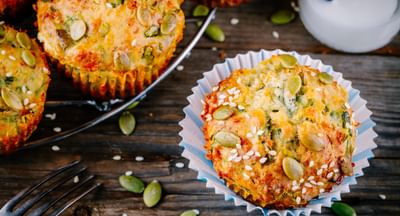 Savory muffins topped with pumpkin seeds and sesame on a rustic wooden table, in blue paper cases.