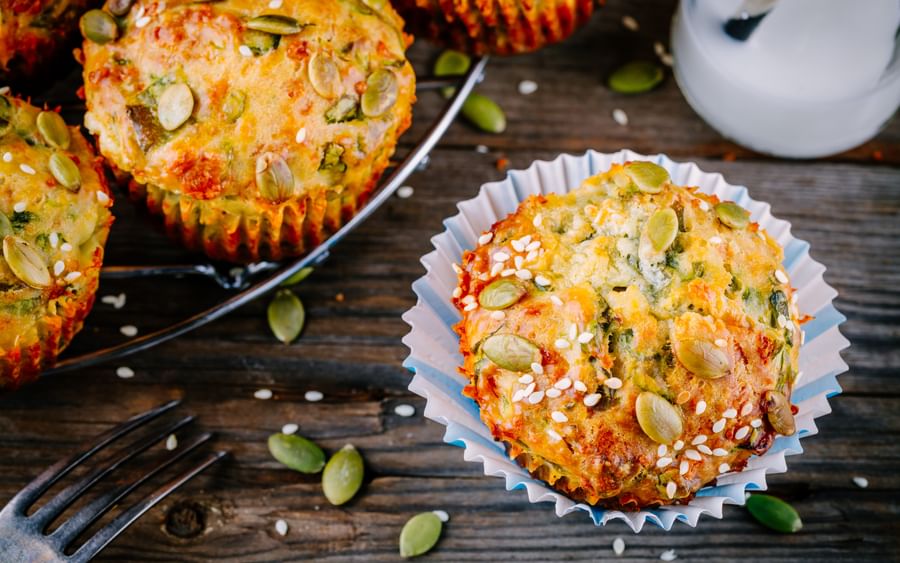 Savory muffins topped with pumpkin seeds and sesame on a rustic wooden table, in blue paper cases.