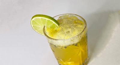 Yellow drink in a crystal-cut glass with foam, lime wedge garnish on rim.