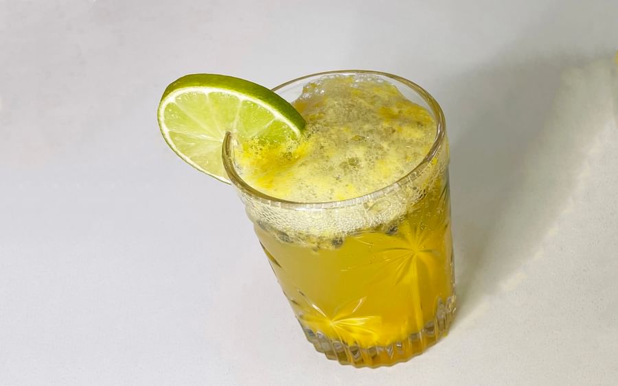 Yellow drink in a crystal-cut glass with foam, lime wedge garnish on rim.