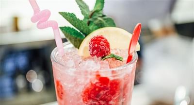 Pink raspberry mocktail in a tall glass with ice, mint, lemon wedge, and pink straw.