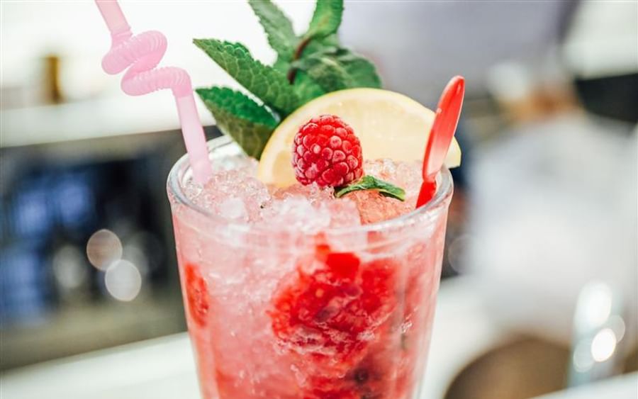 Pink raspberry mocktail in a tall glass with ice, mint, lemon wedge, and pink straw.