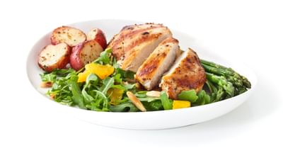 Plate with grilled chicken, roasted potatoes, asparagus, and citrus rocket salad with orange slices.