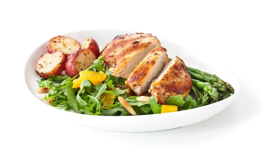 Plate with grilled chicken, roasted potatoes, asparagus, and citrus rocket salad with orange slices.