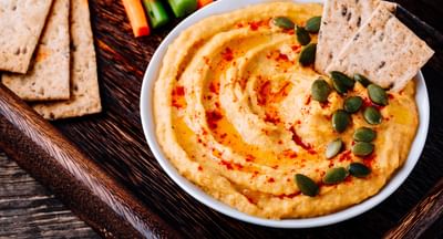 Hummus with paprika and olive oil, topped with pumpkin seeds; pita wedges and carrot-cucumber sticks.