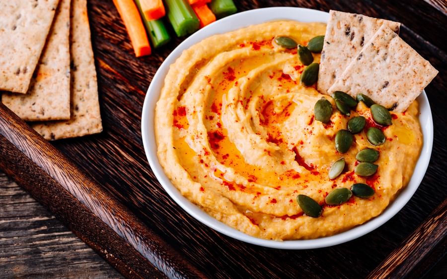 Hummus with paprika and olive oil, topped with pumpkin seeds; pita wedges and carrot-cucumber sticks.