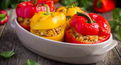 Colourful stuffed bell peppers (red and yellow) with rice filling in a white dish on a wooden table