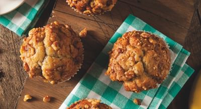 Six nut-topped muffins on a wooden board with a green checkered napkin.
