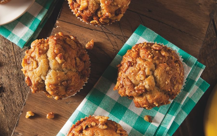 Six nut-topped muffins on a wooden board with a green checkered napkin.