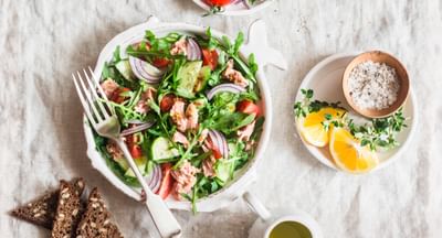 Top-down view of a vibrant tuna salad with greens, tomatoes, cucumber and red onion; lemon on side.