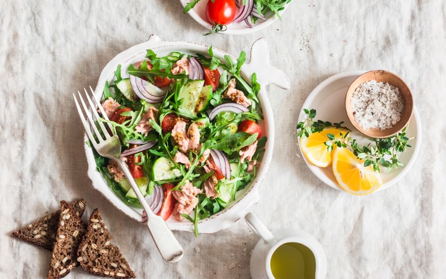 Top-down view of a vibrant tuna salad with greens, tomatoes, cucumber and red onion; lemon on side.