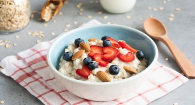 Blue bowl of oatmeal topped with sliced strawberries, blueberries and almonds on a red check cloth.