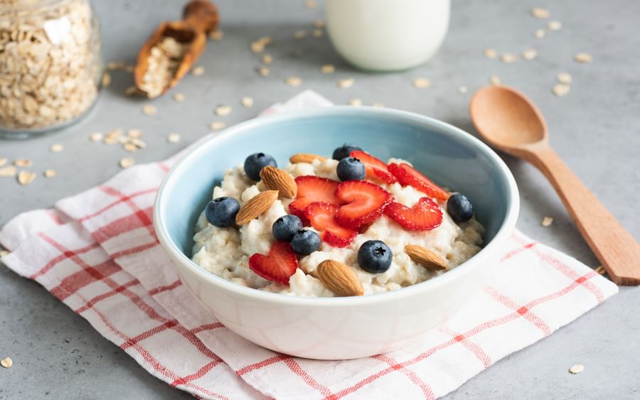 Blue bowl of oatmeal topped with sliced strawberries, blueberries and almonds on a red check cloth.