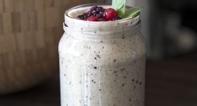 Creamy berry smoothie in a mason jar with a pink straw, mint, and berries on a wooden table.