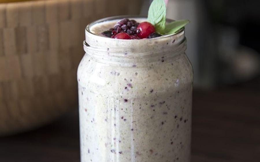 Creamy berry smoothie in a mason jar with a pink straw, mint, and berries on a wooden table.