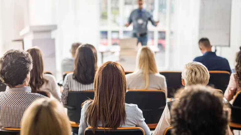 Audience seated in a bright room, watching a presenter at the front giving a talk.