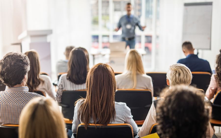 Audience seated in a bright room, watching a presenter at the front giving a talk.