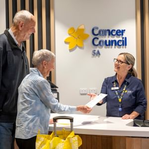 Cancer Council SA reception desk: two older adults hand a document to a staffer.