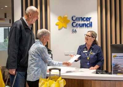 Cancer Council SA reception desk: two older adults hand a document to a staffer.