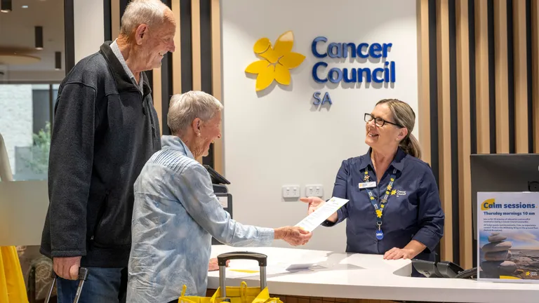 Cancer Council SA reception desk: two older adults hand a document to a staffer.