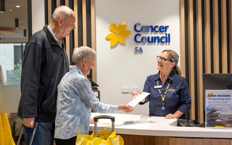 Cancer Council SA reception desk: two older adults hand a document to a staffer.