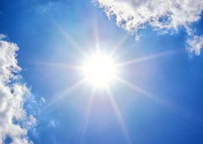 Bright sun with starburst rays in a blue sky and wispy clouds.