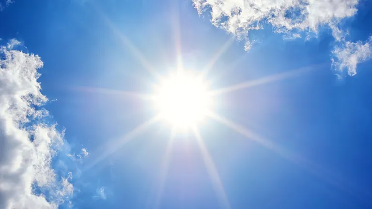 Bright sun with starburst rays in a blue sky and wispy clouds.
