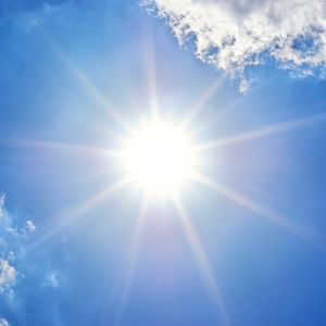 Bright sun with starburst rays in a blue sky and wispy clouds.