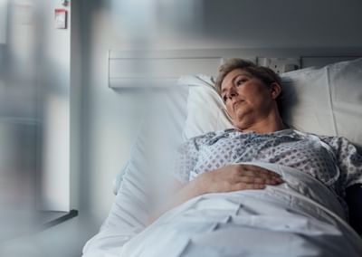 Pregnant person resting in a hospital bed, gazing out a sunlit window in a patient gown.