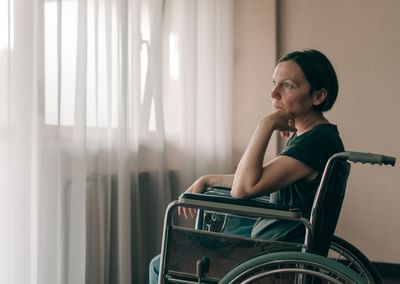 Person in a wheelchair by a sunlit window, resting their chin on their hand.