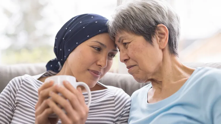 Two people sit close on a couch, heads touching; one wears a navy headscarf, the other in light blue.