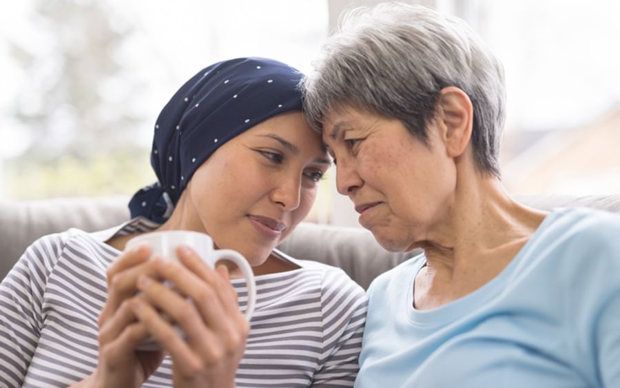 Two people sit close on a couch, heads touching; one wears a navy headscarf, the other in light blue.