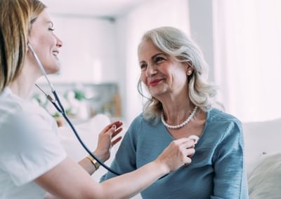 Healthcare worker uses stethoscope on an elderly person in a bright room.