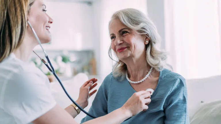 Healthcare worker uses stethoscope on an elderly person in a bright room.