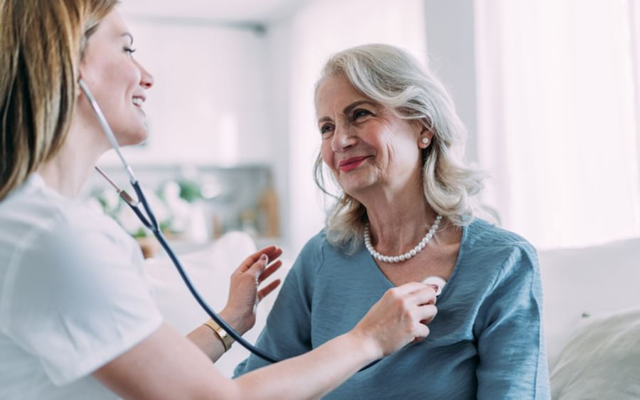 Healthcare worker uses stethoscope on an elderly person in a bright room.